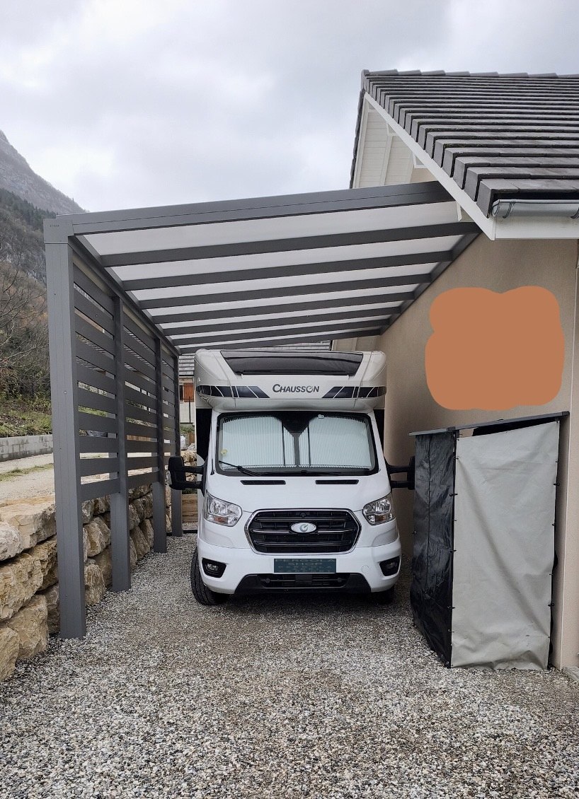 Carport aluminium Skylux adossé abritant un camping-car, fermeture latérale ajourée — pose Top Fermetures