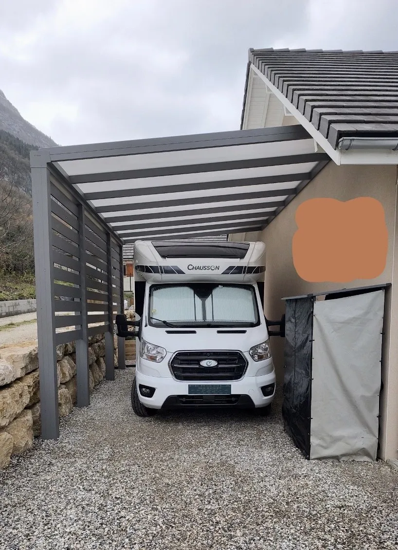 Carport aluminium Skylux adossé abritant un camping-car, fermeture latérale ajourée — pose Top Fermetures